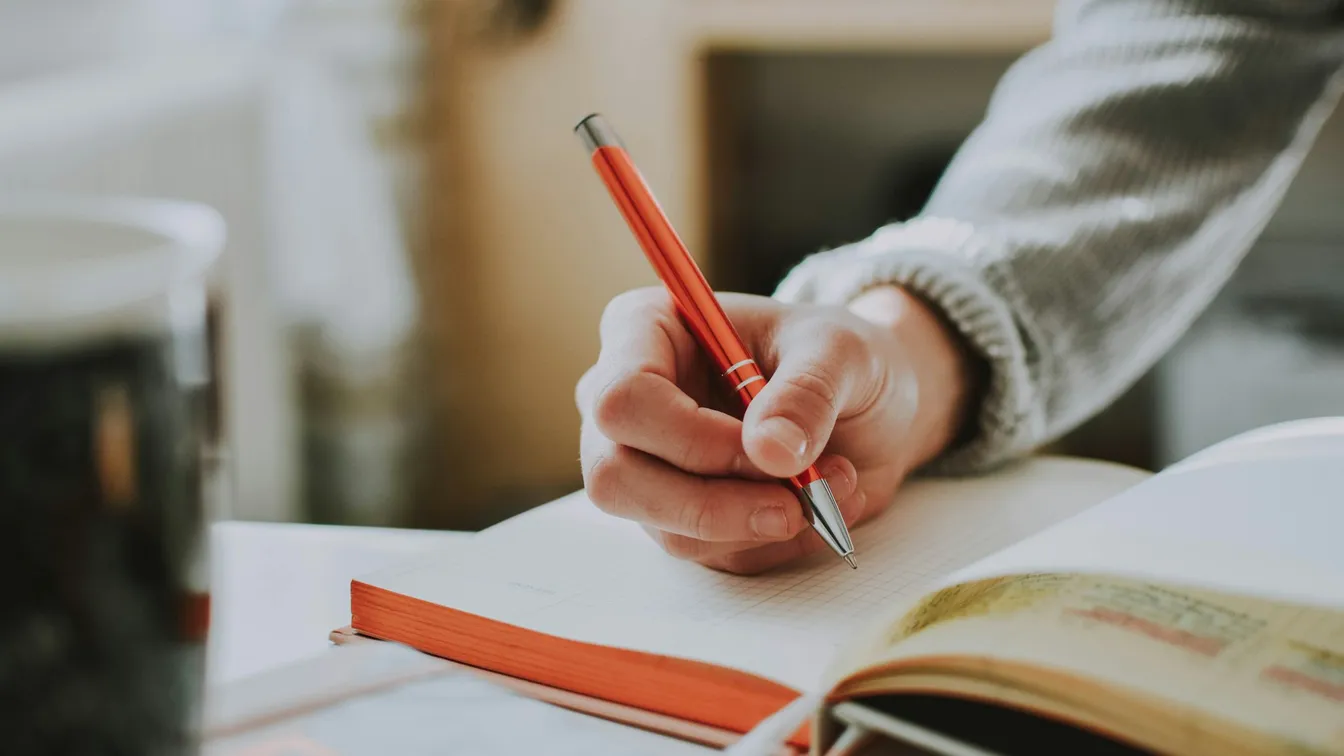 a person writing in a notebook with a pen