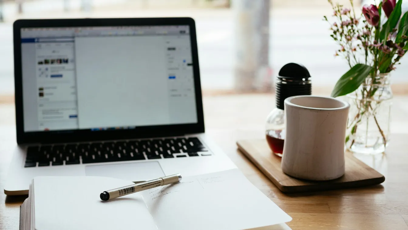 a laptop on a wooden table next to a cup of coffee and a notebook