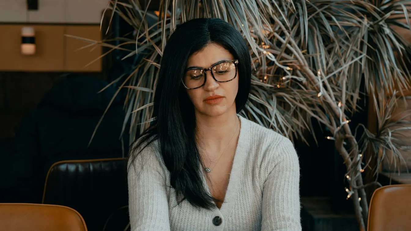 a woman in glasses sitting at a table in a cafe