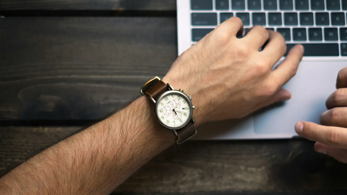 a man's wrist with a watch on top of a laptop