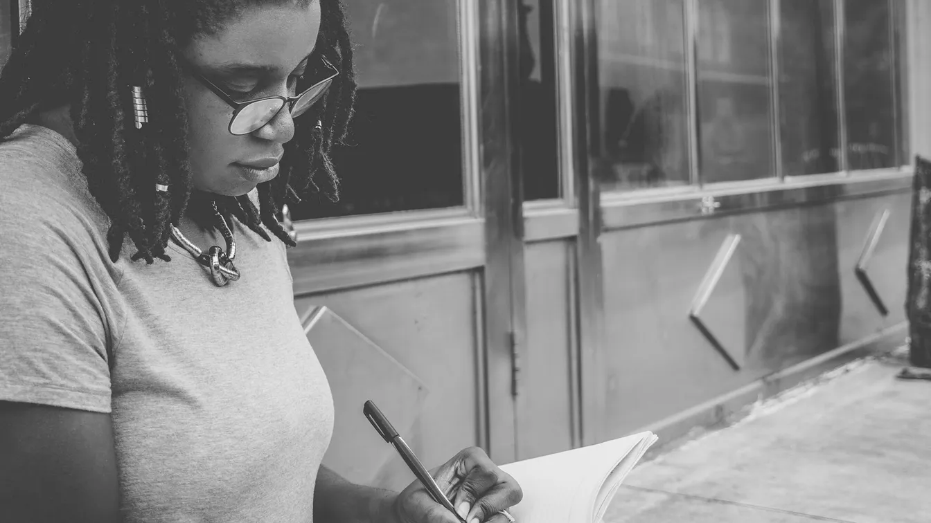 a woman with dreadlocks writing in a notebook