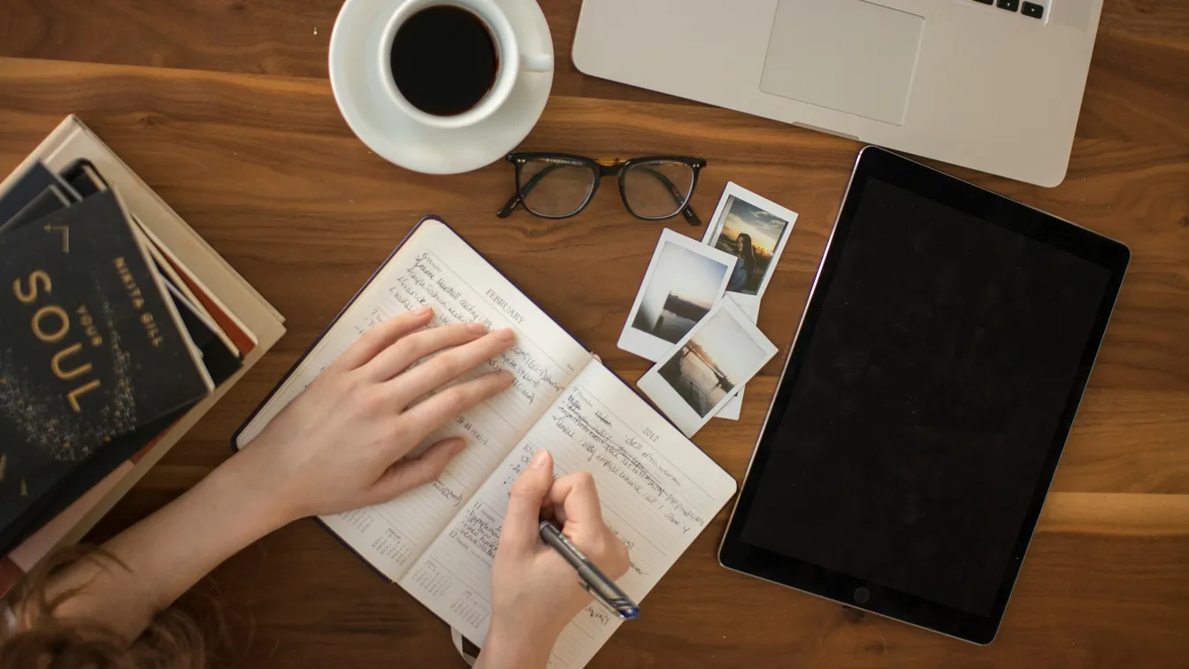 a woman writing in a notebook on a wooden table