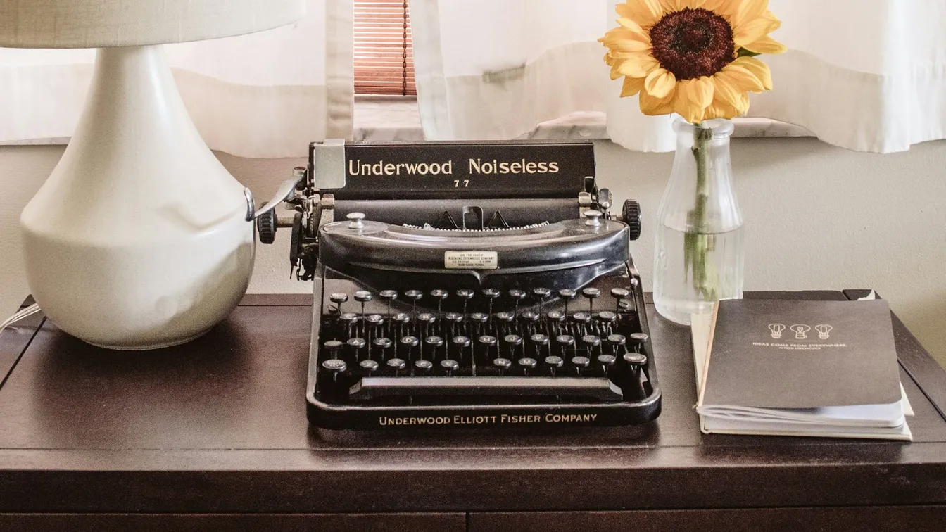 a vintage typewriter sits on a table next to a vase of sunflowers