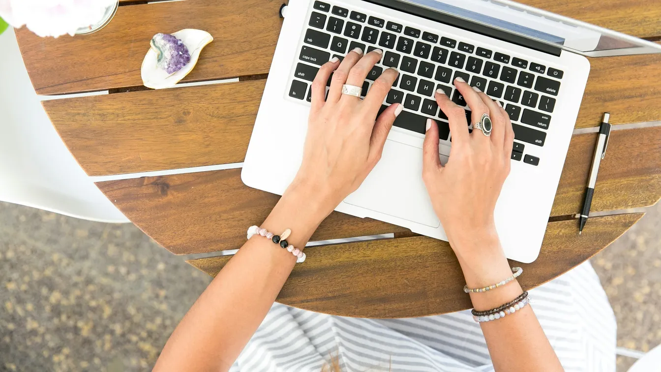 a woman typing on a laptop on a wooden table