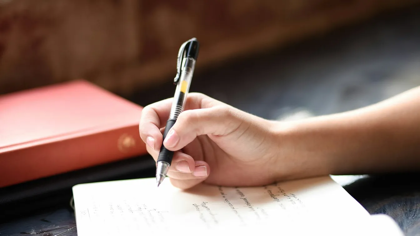 a person writing in a notebook with a pen