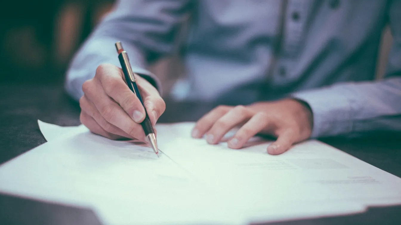 a person signing a document with a pen